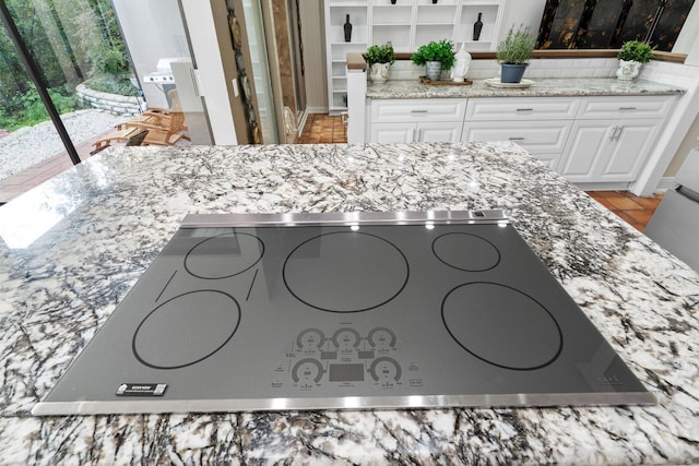 room details with white cabinetry, decorative backsplash, light stone countertops, and black stovetop