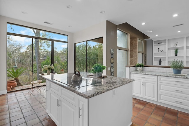 kitchen featuring tasteful backsplash, white cabinetry, a center island, black electric stovetop, and light stone counters