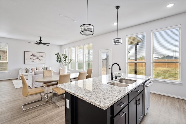 kitchen featuring pendant lighting, sink, light hardwood / wood-style flooring, light stone countertops, and a center island with sink