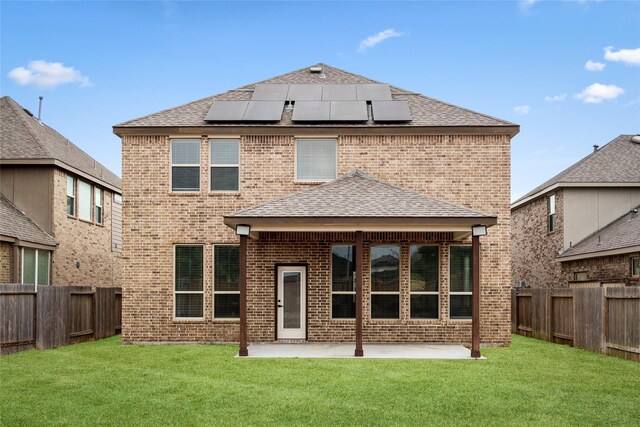 rear view of property featuring a lawn, a patio, and solar panels