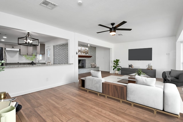 2713 John St, La Marque, TX 77568 - living room with visible vents, a brick fireplace, ceiling fan with notable chandelier, and wood finished floors