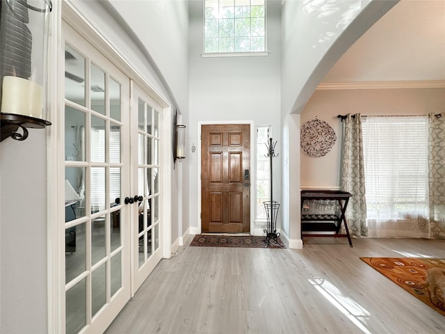 entryway with a towering ceiling, wood-type flooring, ornamental molding, and french doors