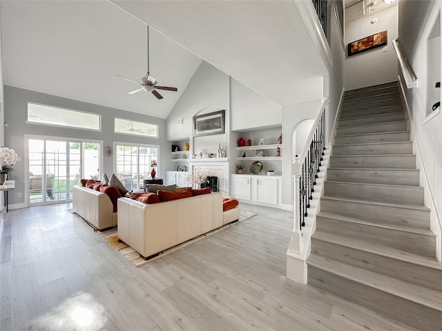 unfurnished living room featuring built in shelves, light hardwood / wood-style flooring, high vaulted ceiling, and ceiling fan