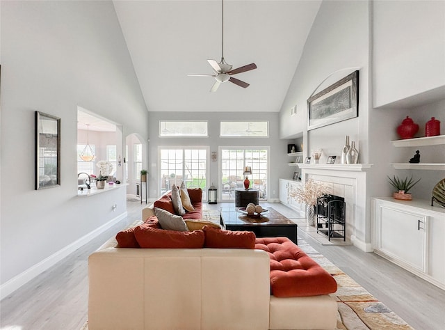 living room with a tiled fireplace, light hardwood / wood-style flooring, high vaulted ceiling, and ceiling fan