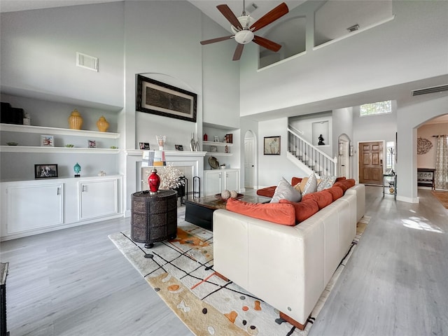 living room featuring a high ceiling, ceiling fan, built in features, and light wood-type flooring