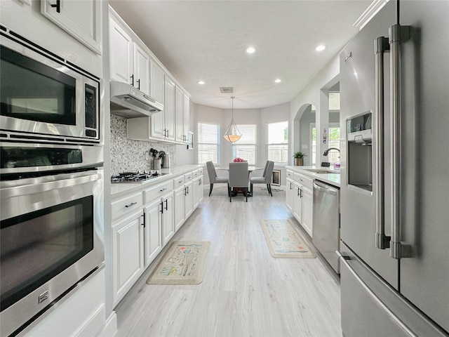 kitchen featuring decorative light fixtures, tasteful backsplash, white cabinets, light hardwood / wood-style floors, and stainless steel appliances