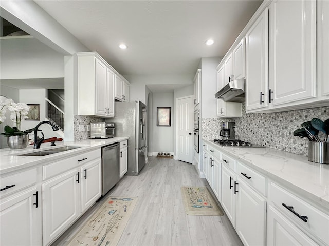 kitchen featuring white cabinetry, sink, stainless steel appliances, light stone countertops, and light wood-type flooring