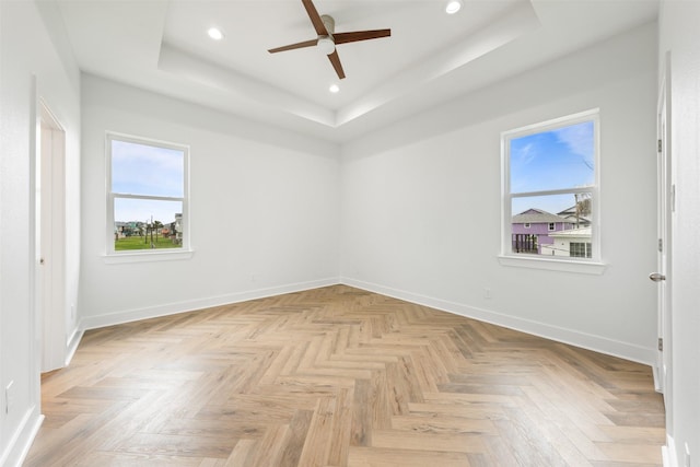 empty room featuring a raised ceiling, light parquet flooring, and ceiling fan