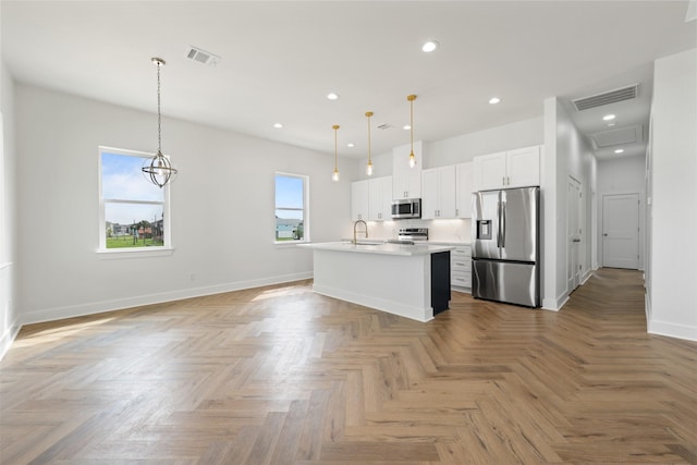 kitchen with stainless steel appliances, white cabinetry, a center island with sink, and decorative light fixtures