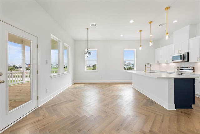 kitchen with sink, hanging light fixtures, a center island with sink, stainless steel appliances, and white cabinets