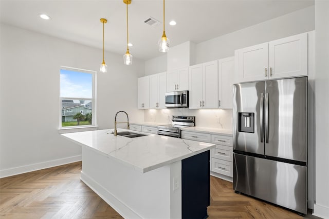 kitchen featuring sink, light stone counters, an island with sink, stainless steel appliances, and white cabinets