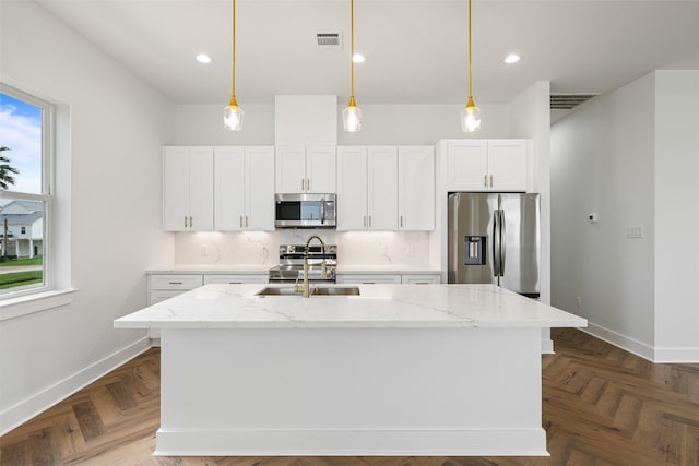 kitchen featuring stainless steel appliances, white cabinetry, a kitchen island with sink, and light stone counters