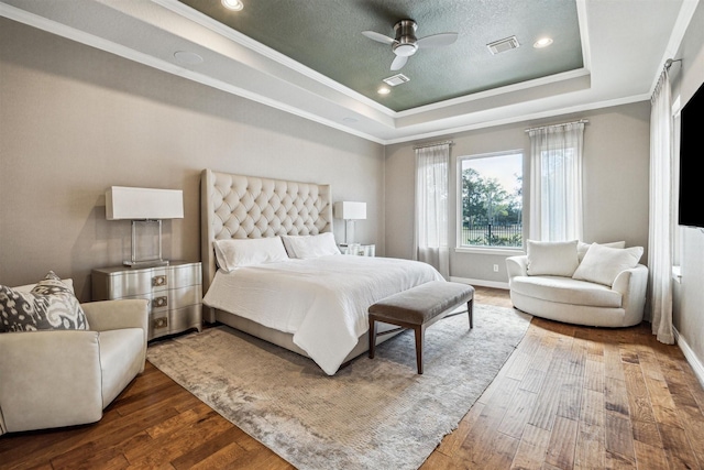 bedroom featuring ceiling fan, hardwood / wood-style floors, ornamental molding, a textured ceiling, and a raised ceiling