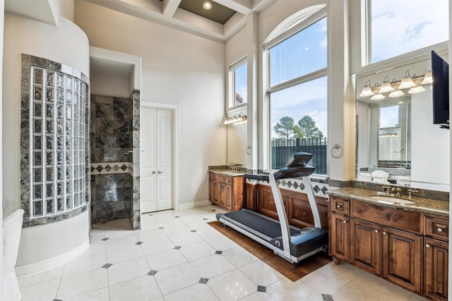 bathroom with a healthy amount of sunlight, a towering ceiling, vanity, and tiled shower