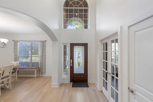 foyer entrance featuring crown molding, a towering ceiling, a notable chandelier, and light hardwood / wood-style floors