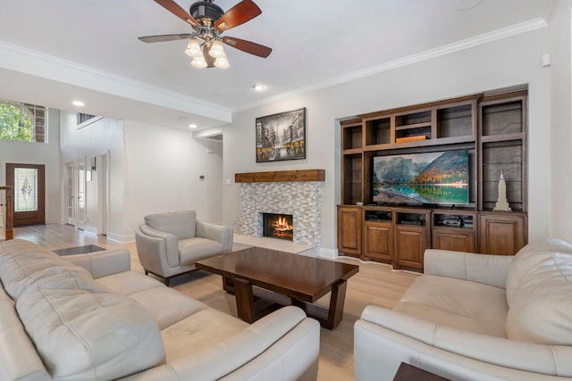 living room with ceiling fan, ornamental molding, a tiled fireplace, and light hardwood / wood-style flooring