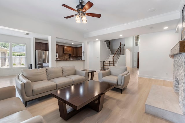 living room featuring ceiling fan, a stone fireplace, and light hardwood / wood-style flooring