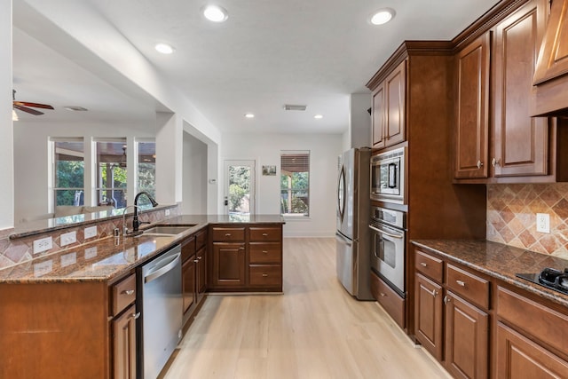 kitchen featuring sink, light hardwood / wood-style flooring, dark stone countertops, appliances with stainless steel finishes, and kitchen peninsula