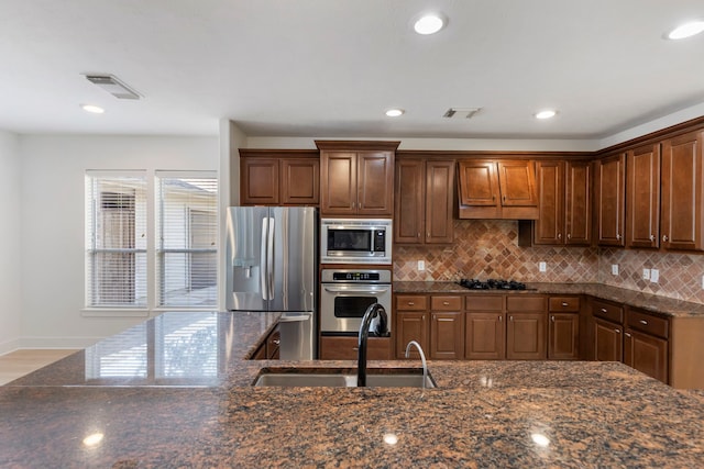 kitchen featuring stainless steel appliances, sink, dark stone counters, and decorative backsplash