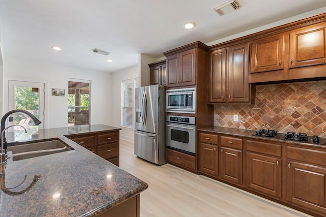 kitchen with sink, tasteful backsplash, dark stone countertops, appliances with stainless steel finishes, and light hardwood / wood-style floors