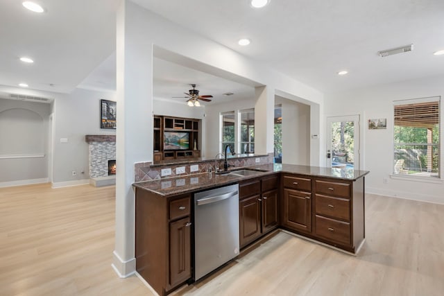 kitchen featuring sink, a fireplace, stainless steel dishwasher, kitchen peninsula, and dark stone counters