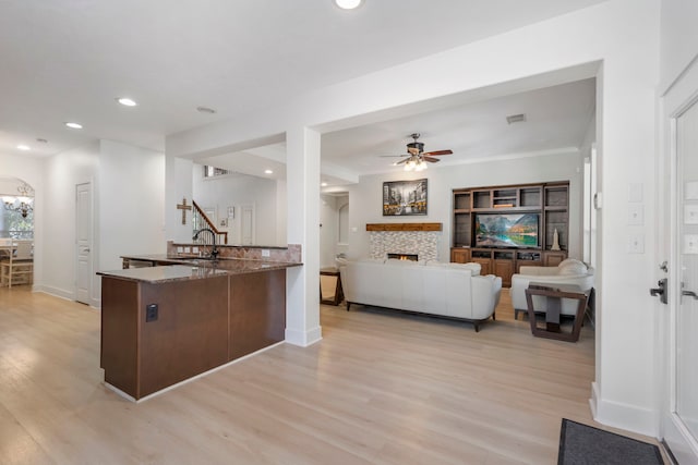 kitchen with sink, stone counters, ceiling fan with notable chandelier, kitchen peninsula, and light wood-type flooring