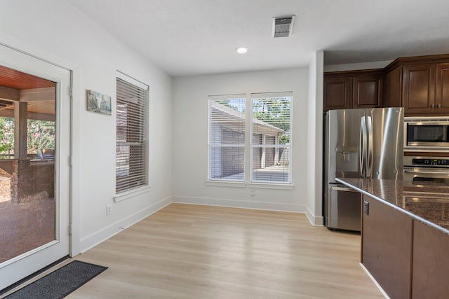 kitchen featuring appliances with stainless steel finishes, light hardwood / wood-style floors, dark brown cabinets, and dark stone countertops