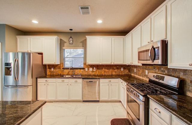 kitchen with appliances with stainless steel finishes, decorative light fixtures, sink, white cabinets, and dark stone counters