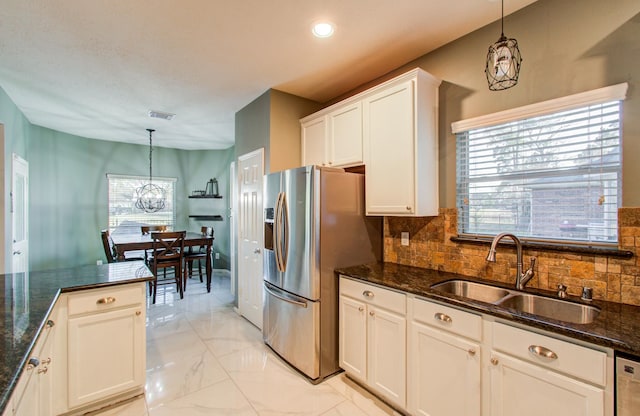 kitchen with stainless steel fridge, sink, white cabinets, and decorative light fixtures