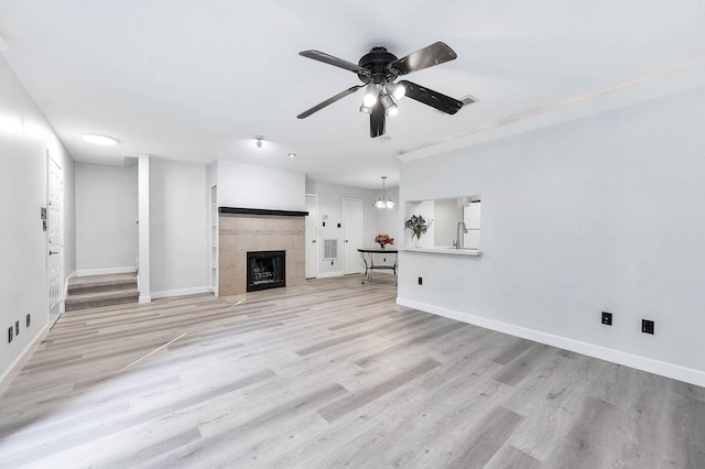 unfurnished living room featuring ceiling fan, a tiled fireplace, sink, and light wood-type flooring