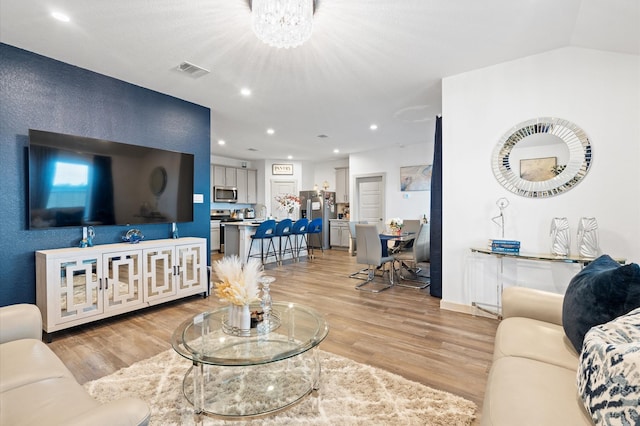 living room with lofted ceiling, a notable chandelier, and light wood-type flooring