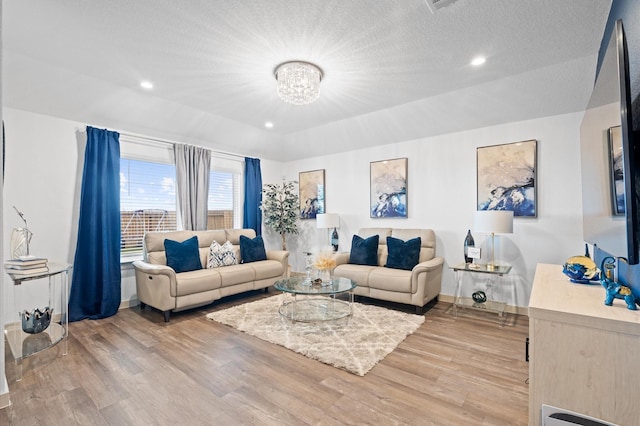 living room with a notable chandelier, light hardwood / wood-style flooring, and a textured ceiling