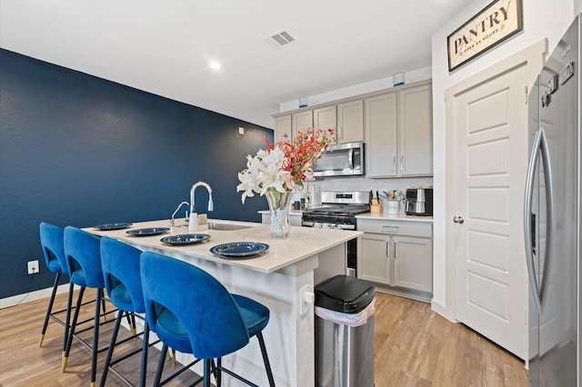 kitchen with gray cabinets, a breakfast bar, a kitchen island with sink, stainless steel appliances, and light hardwood / wood-style flooring