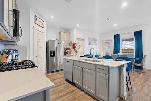 kitchen with sink, light hardwood / wood-style flooring, a kitchen breakfast bar, stainless steel appliances, and an island with sink