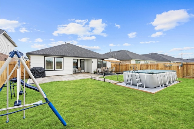 rear view of house featuring a playground, a patio, a covered pool, and a yard