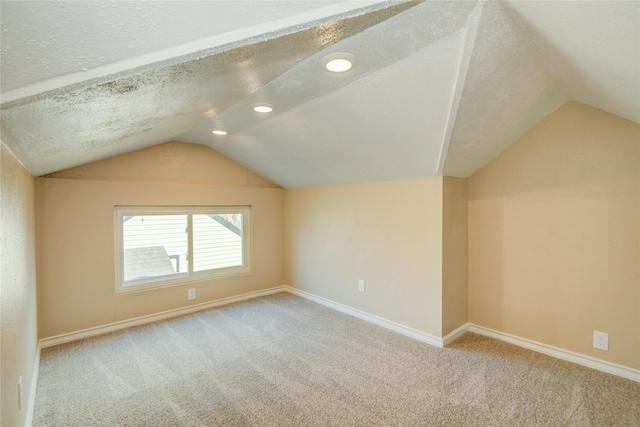 additional living space featuring vaulted ceiling, light colored carpet, and a textured ceiling