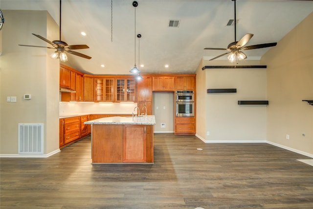 kitchen featuring sink, light stone counters, an island with sink, dark hardwood / wood-style flooring, and stainless steel double oven