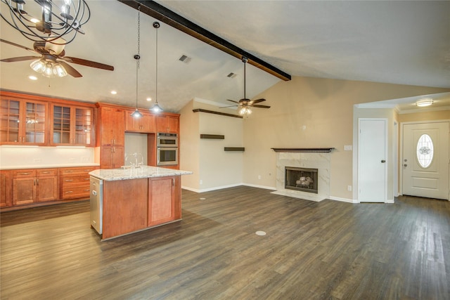 kitchen featuring vaulted ceiling with beams, dark hardwood / wood-style floors, light stone countertops, a center island with sink, and stainless steel double oven