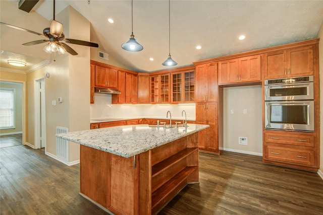 kitchen with sink, double oven, light stone counters, a center island with sink, and dark hardwood / wood-style flooring