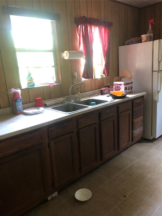 kitchen with white refrigerator, sink, a wealth of natural light, and wood walls