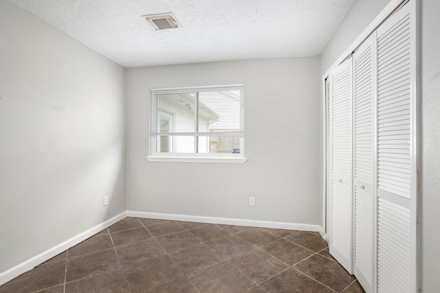 unfurnished bedroom featuring dark tile patterned flooring, a closet, and a textured ceiling