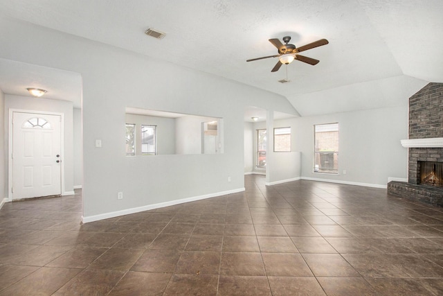 unfurnished living room with ceiling fan, a fireplace, vaulted ceiling, and dark tile patterned floors