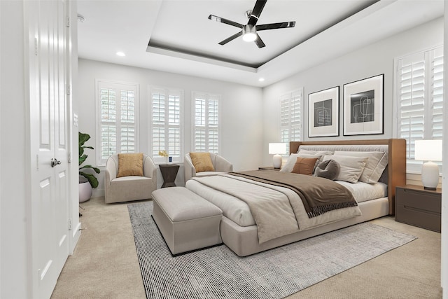 bedroom featuring ceiling fan, light colored carpet, and a raised ceiling