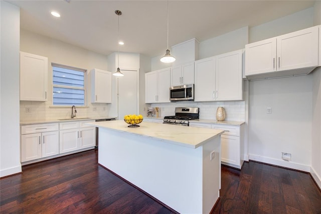 kitchen featuring baseboards, dark wood-style floors, appliances with stainless steel finishes, a center island, and white cabinetry