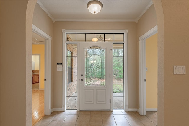 entryway with arched walkways, crown molding, baseboards, and light tile patterned floors