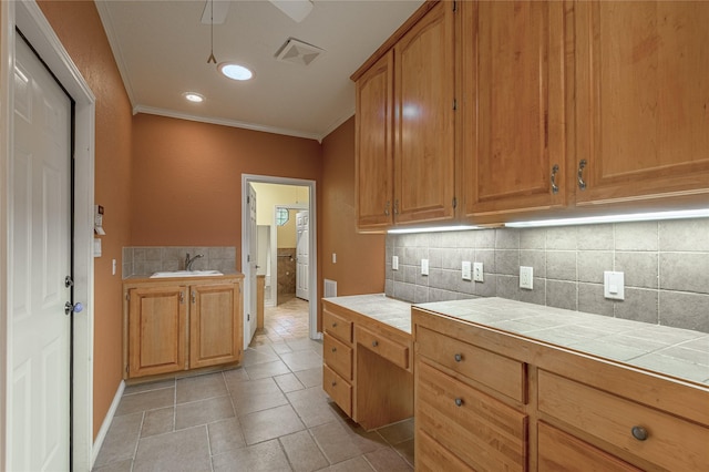 kitchen featuring tasteful backsplash, visible vents, tile countertops, crown molding, and a sink