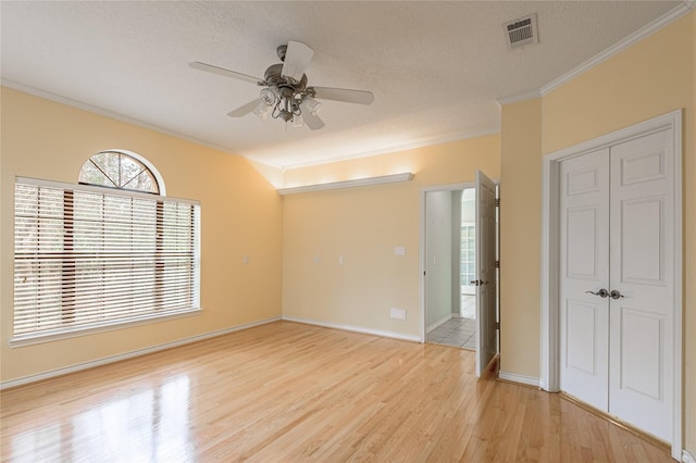 unfurnished room with a textured ceiling, light wood-style flooring, visible vents, baseboards, and ornamental molding