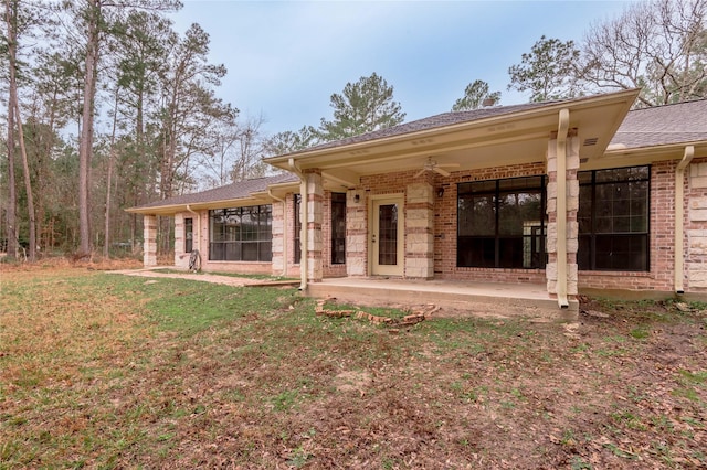 rear view of house featuring brick siding, a shingled roof, a ceiling fan, a lawn, and a patio area