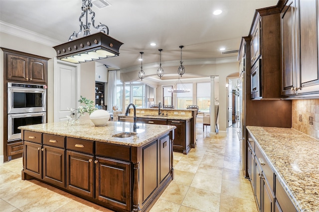 kitchen featuring a center island with sink, sink, pendant lighting, and light stone counters