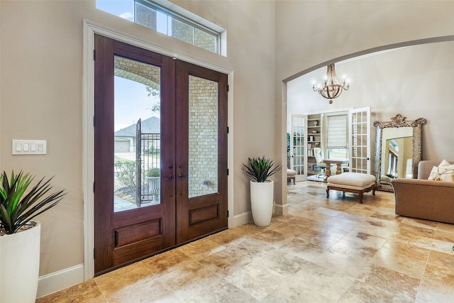 foyer entrance featuring a high ceiling, a healthy amount of sunlight, a notable chandelier, and french doors